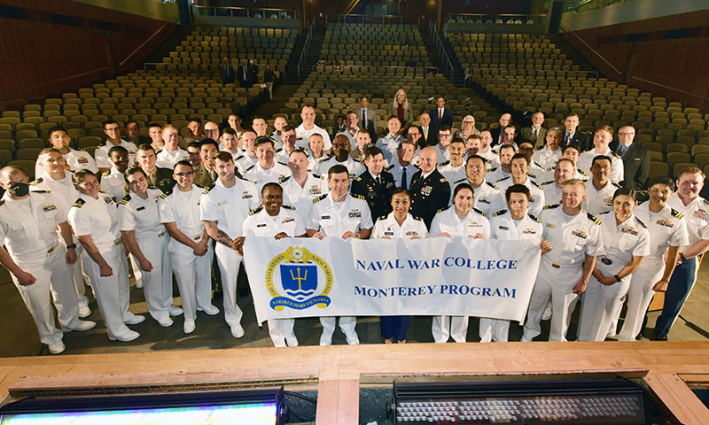 The 91st graduating class of the Naval War College Monterey partnership with the Naval Postgraduate School for Joint Professional Military Education stands for a group portrait in King Hall, June 9. 